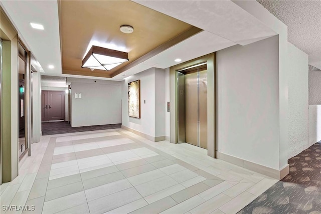 corridor with a raised ceiling, elevator, and light tile patterned floors