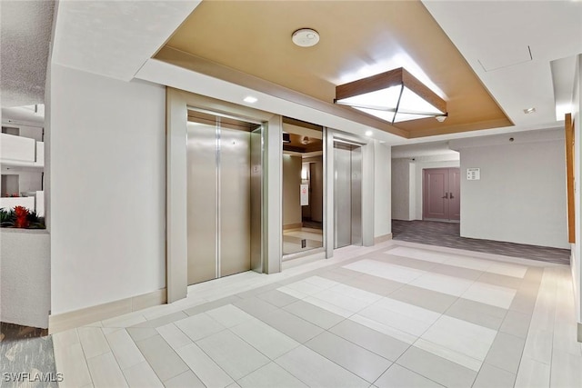 spare room with elevator, a tray ceiling, and light tile patterned flooring