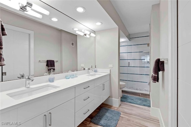 bathroom with hardwood / wood-style flooring, vanity, toilet, and tiled shower