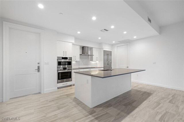 kitchen featuring white cabinetry, sink, wall chimney exhaust hood, a kitchen island with sink, and appliances with stainless steel finishes