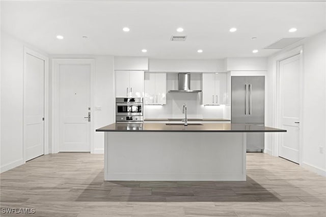 kitchen featuring appliances with stainless steel finishes, sink, wall chimney range hood, a center island with sink, and white cabinets