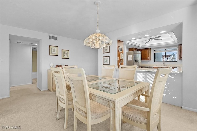 dining area with ceiling fan with notable chandelier, light colored carpet, a raised ceiling, and sink