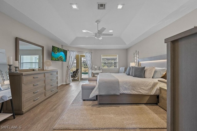 bedroom featuring access to exterior, light wood-type flooring, a raised ceiling, and ceiling fan