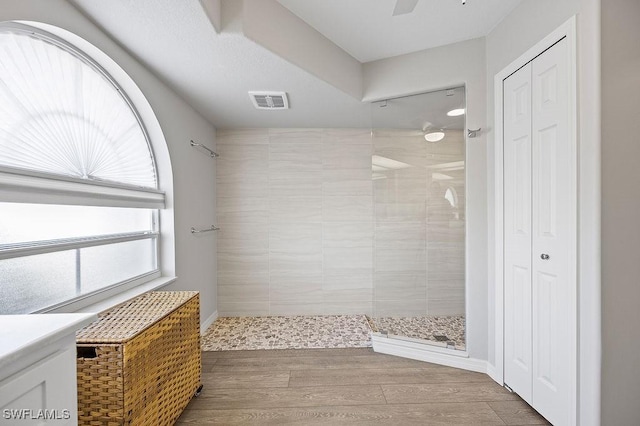 bathroom with ceiling fan, a tile shower, and wood-type flooring