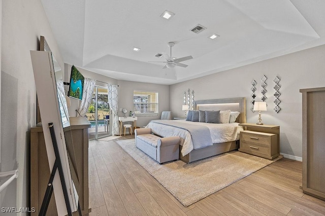 bedroom with ceiling fan, light hardwood / wood-style floors, access to exterior, and a tray ceiling