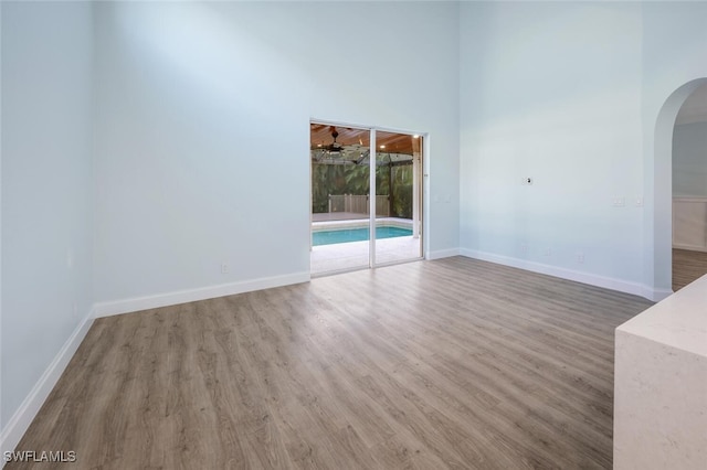 empty room with ceiling fan, wood-type flooring, and a high ceiling