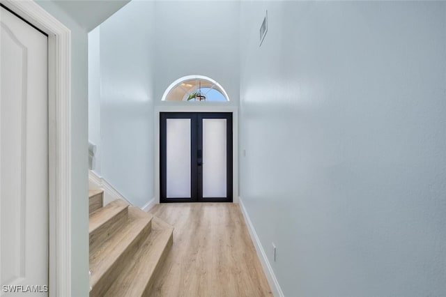 foyer featuring light hardwood / wood-style flooring, a high ceiling, and french doors