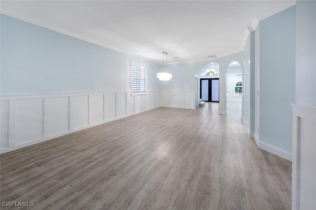 spare room with an inviting chandelier, ornamental molding, and light wood-type flooring