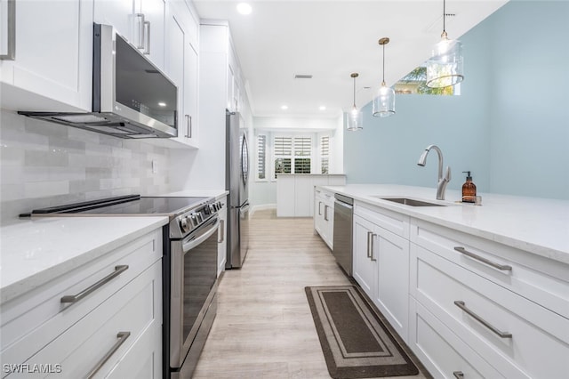 kitchen featuring white cabinets, light wood-type flooring, hanging light fixtures, and appliances with stainless steel finishes