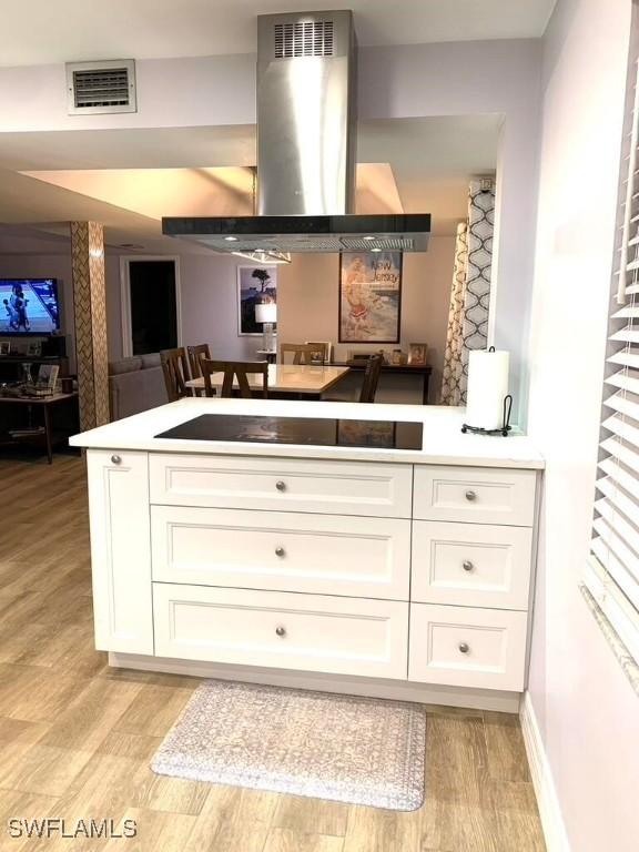 kitchen featuring white cabinets, black electric stovetop, light hardwood / wood-style floors, and exhaust hood