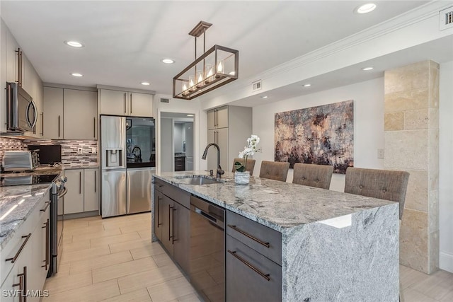 kitchen with stainless steel appliances, a kitchen island with sink, sink, decorative light fixtures, and gray cabinets