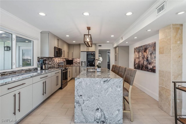 kitchen with a kitchen bar, stainless steel appliances, a kitchen island with sink, decorative light fixtures, and gray cabinets