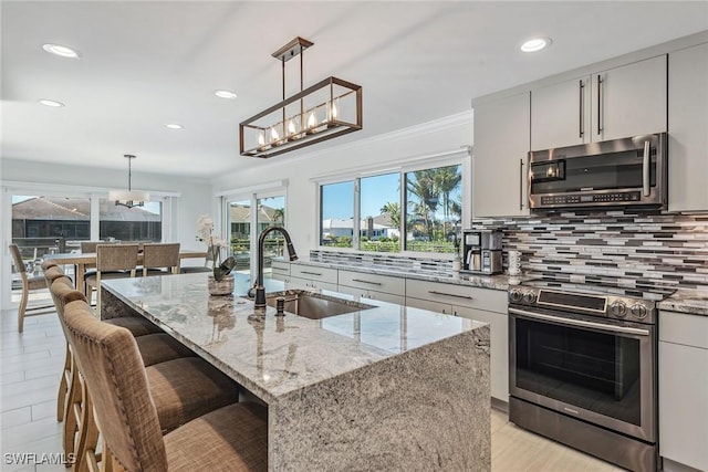 kitchen featuring appliances with stainless steel finishes, sink, decorative light fixtures, and an island with sink