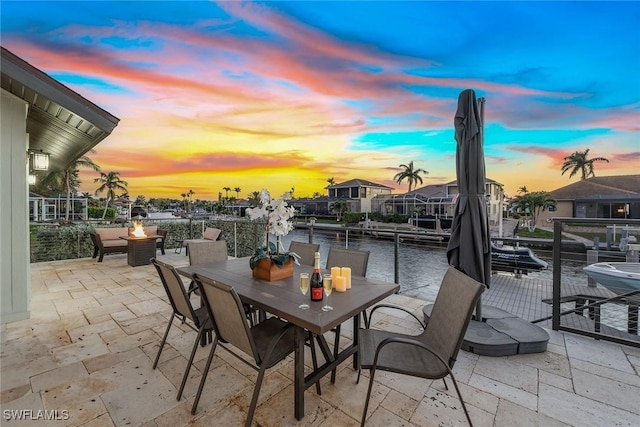 patio terrace at dusk featuring a fire pit, a water view, and a dock