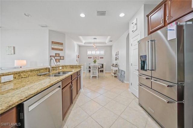 kitchen with sink, light tile patterned floors, a tray ceiling, light stone counters, and stainless steel appliances