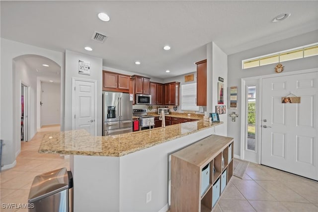 kitchen featuring stainless steel appliances, light stone counters, kitchen peninsula, a kitchen bar, and light tile patterned flooring