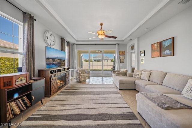 tiled living room featuring a raised ceiling, ceiling fan, and plenty of natural light