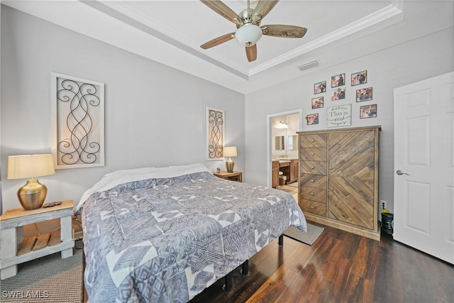 bedroom featuring dark hardwood / wood-style flooring, a tray ceiling, ceiling fan, crown molding, and connected bathroom