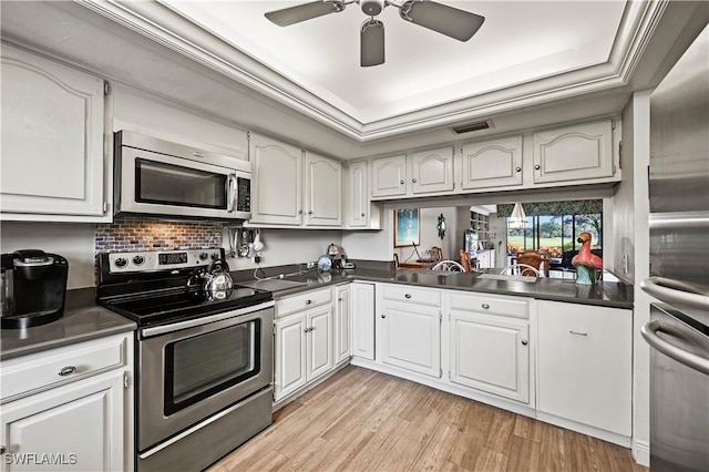 kitchen with light hardwood / wood-style flooring, ceiling fan, appliances with stainless steel finishes, a tray ceiling, and white cabinets