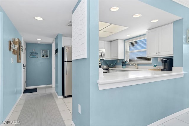 kitchen with sink, kitchen peninsula, appliances with stainless steel finishes, light tile patterned flooring, and white cabinetry