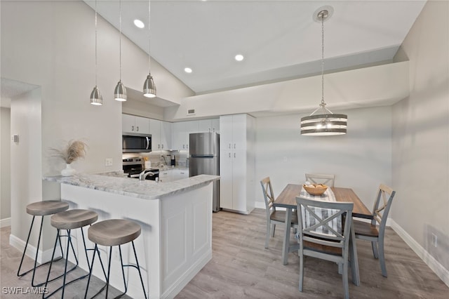 kitchen with white cabinetry, hanging light fixtures, high vaulted ceiling, and stainless steel appliances