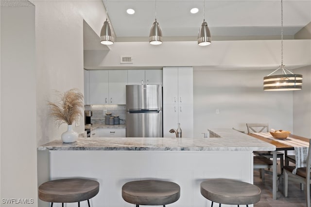 kitchen with stainless steel fridge, dark hardwood / wood-style flooring, white cabinetry, and a breakfast bar area