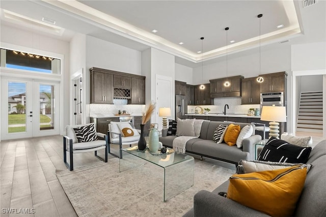 living room featuring french doors, sink, light hardwood / wood-style flooring, a towering ceiling, and a tray ceiling