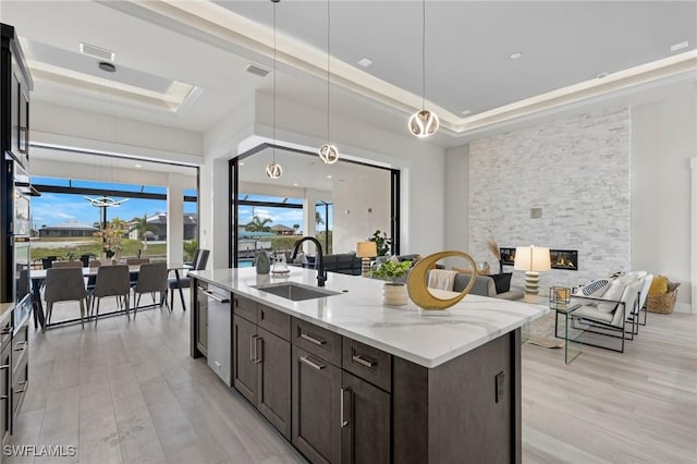 kitchen featuring a stone fireplace, sink, light stone countertops, a tray ceiling, and light hardwood / wood-style floors