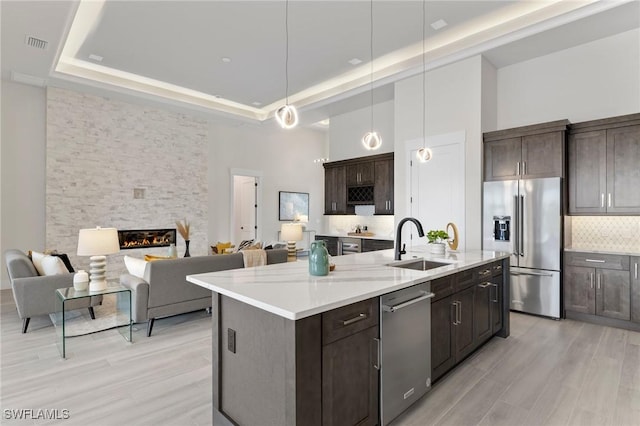 kitchen featuring sink, stainless steel appliances, a raised ceiling, a towering ceiling, and a kitchen island with sink