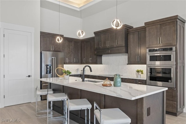 kitchen featuring sink, a kitchen island with sink, dark brown cabinets, appliances with stainless steel finishes, and light wood-type flooring