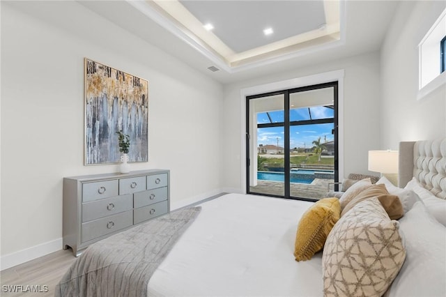 bedroom featuring a raised ceiling, light hardwood / wood-style flooring, and multiple windows