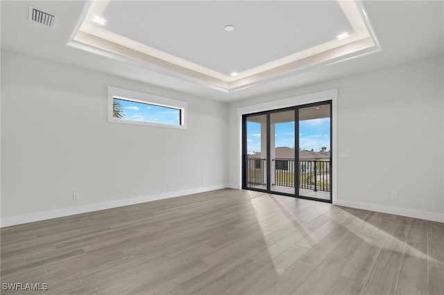 spare room with light wood-type flooring and a tray ceiling