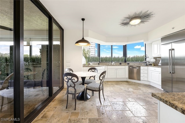 kitchen with white cabinets, decorative light fixtures, stainless steel appliances, and dark stone countertops