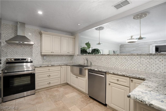 kitchen featuring appliances with stainless steel finishes, sink, wall chimney range hood, cream cabinets, and hanging light fixtures