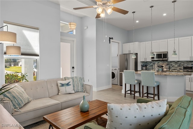 living room with a high ceiling, washer / clothes dryer, light hardwood / wood-style flooring, and ceiling fan