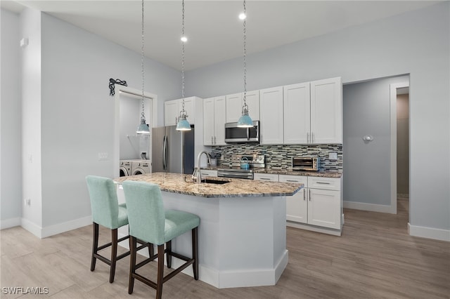 kitchen with light stone countertops, sink, stainless steel appliances, a center island with sink, and washer and dryer