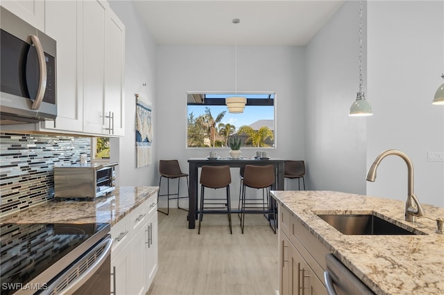 kitchen featuring light wood-type flooring, stainless steel appliances, sink, pendant lighting, and white cabinetry