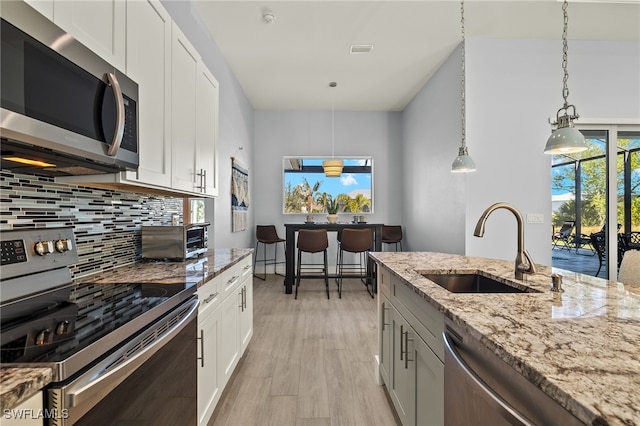 kitchen featuring appliances with stainless steel finishes, light stone counters, sink, pendant lighting, and white cabinets