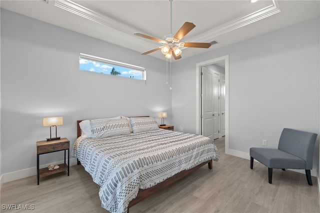 bedroom featuring ceiling fan, a raised ceiling, ornamental molding, and light hardwood / wood-style flooring