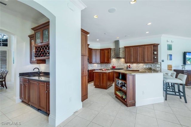 kitchen featuring sink, wall chimney exhaust hood, kitchen peninsula, crown molding, and light tile patterned floors