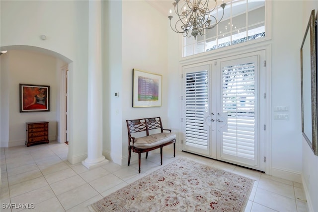 tiled entrance foyer featuring decorative columns, french doors, a high ceiling, and an inviting chandelier