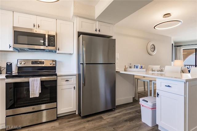 kitchen with kitchen peninsula, dark hardwood / wood-style flooring, backsplash, stainless steel appliances, and white cabinetry