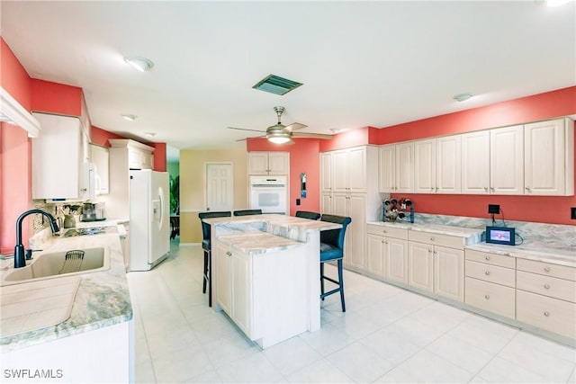 kitchen with white appliances, a kitchen breakfast bar, sink, ceiling fan, and a kitchen island