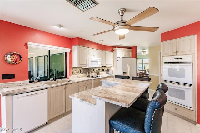 kitchen with white appliances, backsplash, sink, light stone counters, and a breakfast bar area