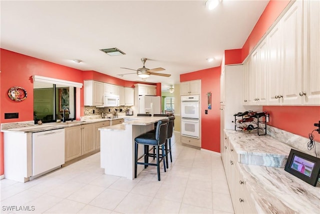 kitchen with ceiling fan, sink, white appliances, a breakfast bar, and a kitchen island