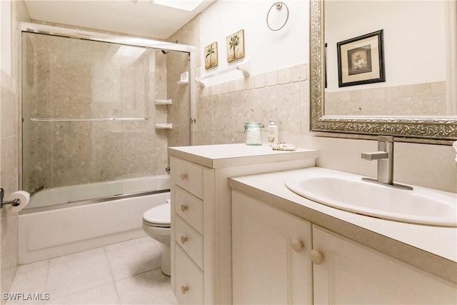 full bathroom with tile patterned flooring, combined bath / shower with glass door, toilet, vanity, and tile walls