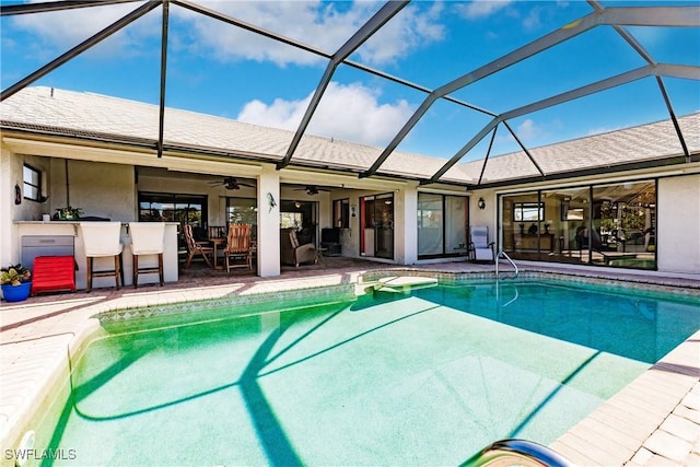 view of pool with an outdoor bar, a patio, glass enclosure, and ceiling fan