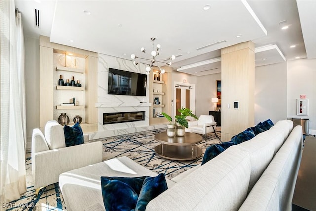 living room featuring built in shelves, a premium fireplace, and an inviting chandelier