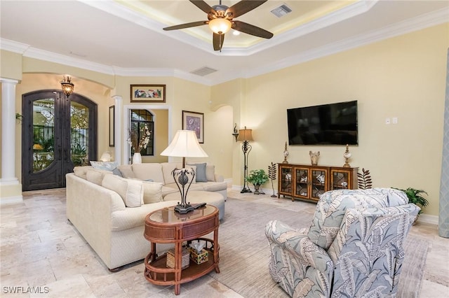 living room featuring ceiling fan, decorative columns, a raised ceiling, and ornamental molding