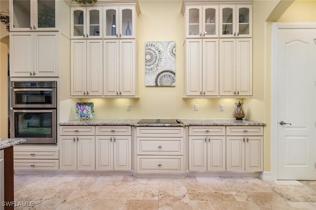 kitchen with stainless steel double oven, light stone counters, and black electric stovetop